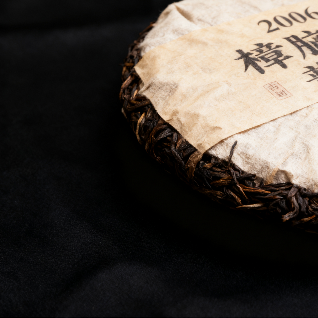 Close-up of a compressed Pu-erh tea cake wrapped in paper with Chinese characters and the year 2006.