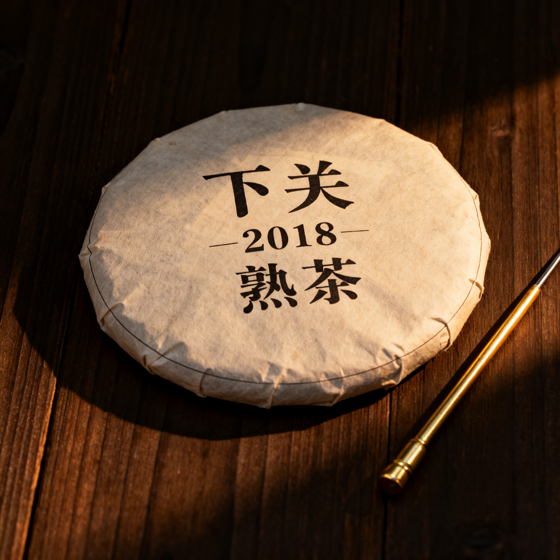 Xiaguan 2018 ripe Pu-erh tea cake on wooden surface with gold tea needle