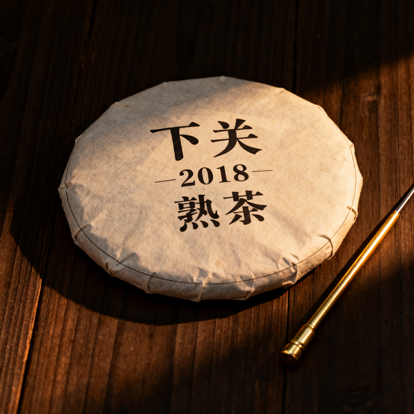 Xiaguan 2018 ripe Pu-erh tea cake on wooden surface with gold tea needle