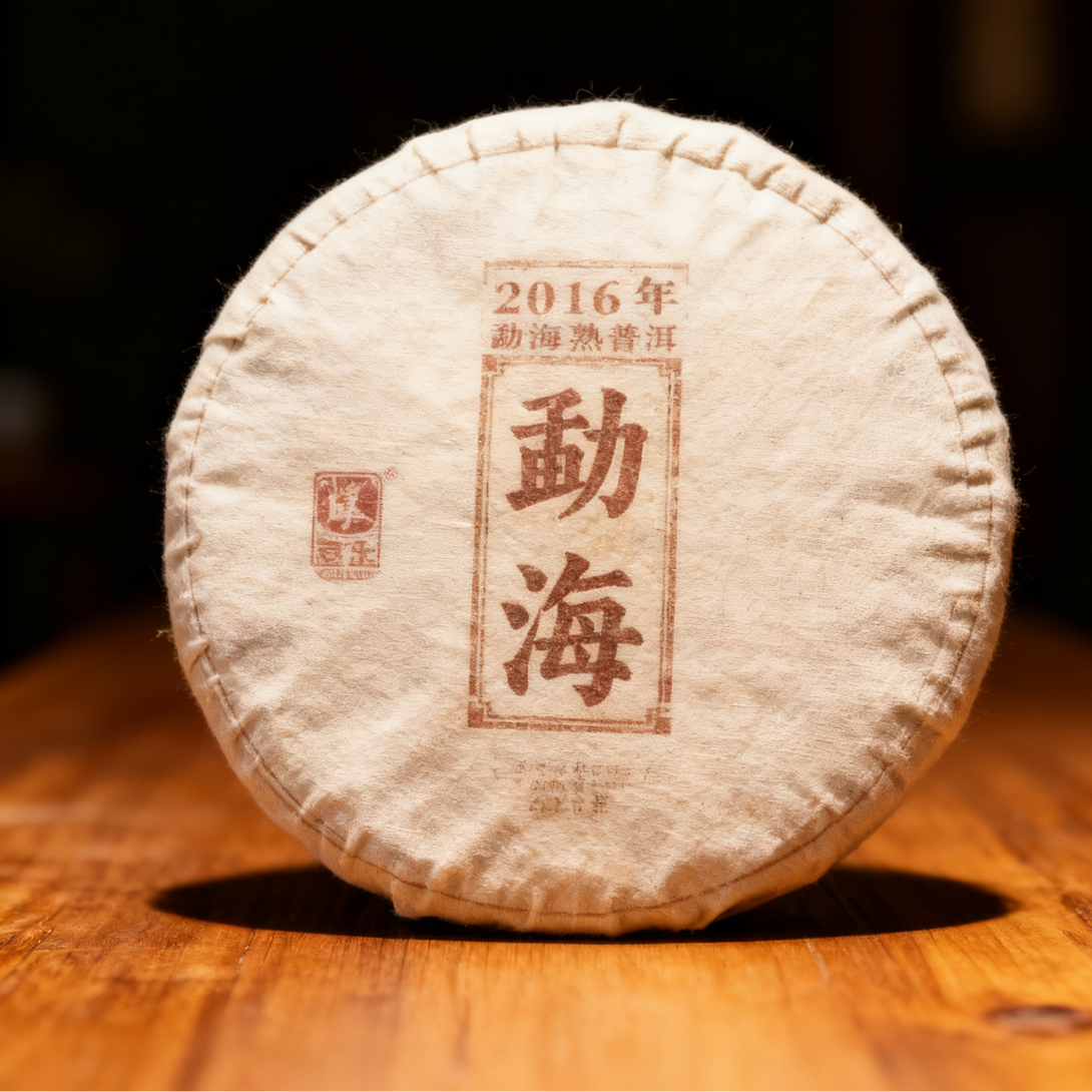 2016 Menghai ripe Pu-erh tea cake in traditional cloth wrapping on wooden table.
