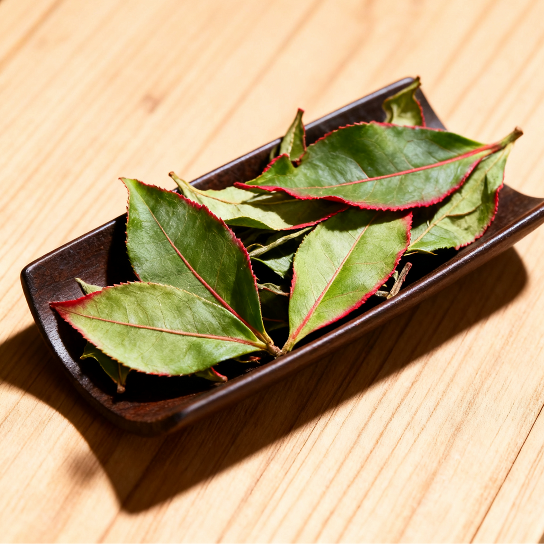Fresh tea leaves in a small brown dish, placed on a wooden surface.
