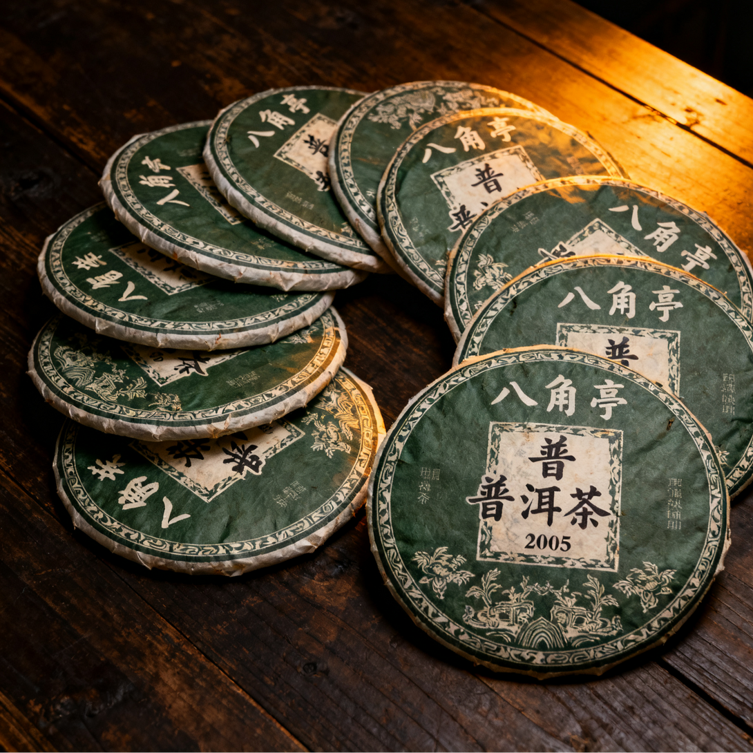 Stack of wrapped Pu-erh tea cakes with green packaging labeled 'Bajiao Ting Pu-erh Tea 2005' on a wooden table