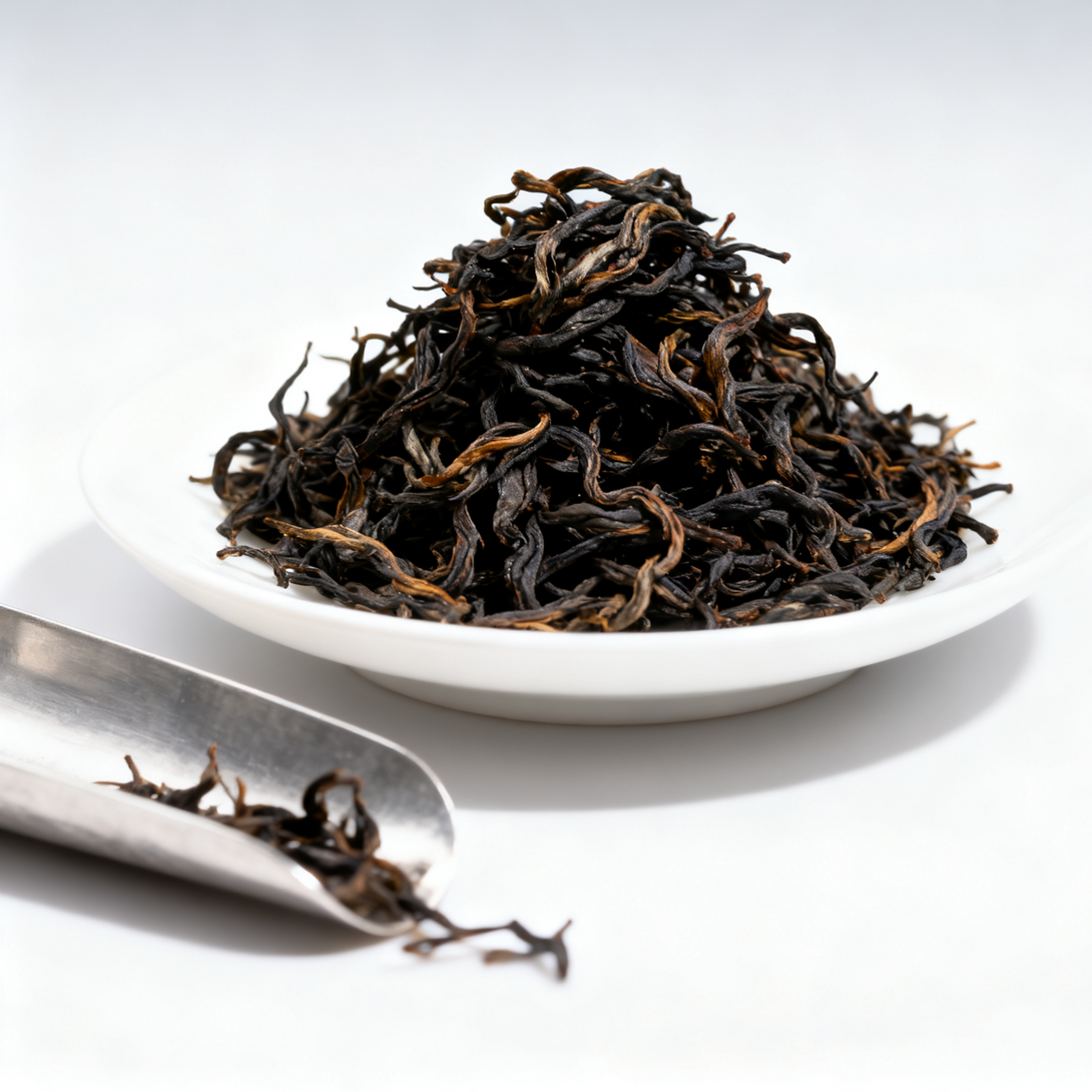 Loose black tea leaves piled on a white plate, with a metal scoop beside them.