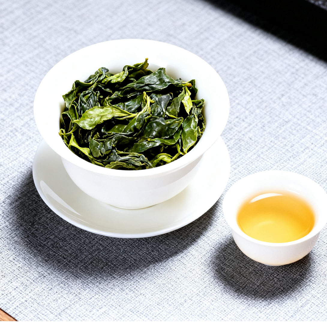 Fresh green tea leaves in white porcelain bowl with cup of hot brewed tea on gray fabric background, organic loose leaf tea